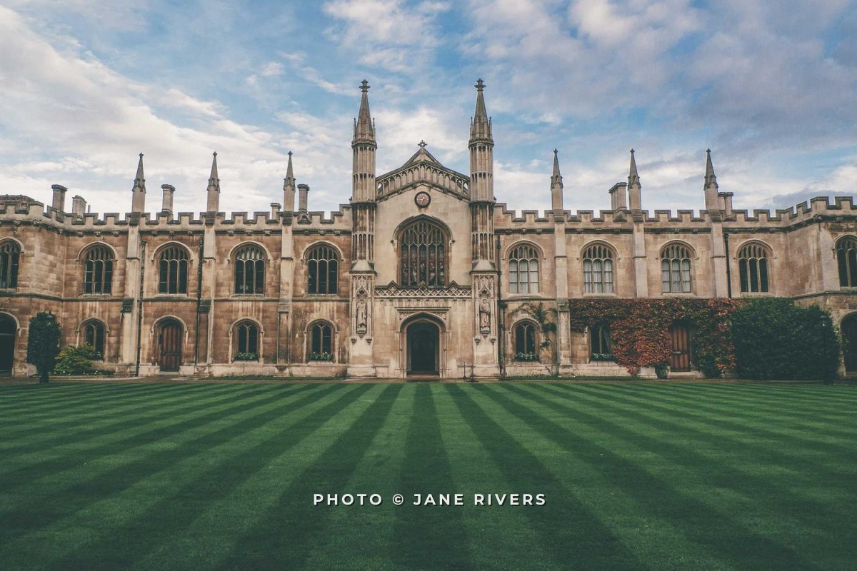 A symmetrical college building with a striped lawn and a small spaced-capitals credit centered at the bottom