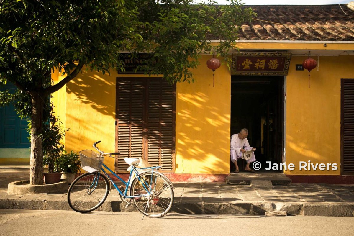 A yellow shopfront photo where the watermark covers a man sitting in the doorway