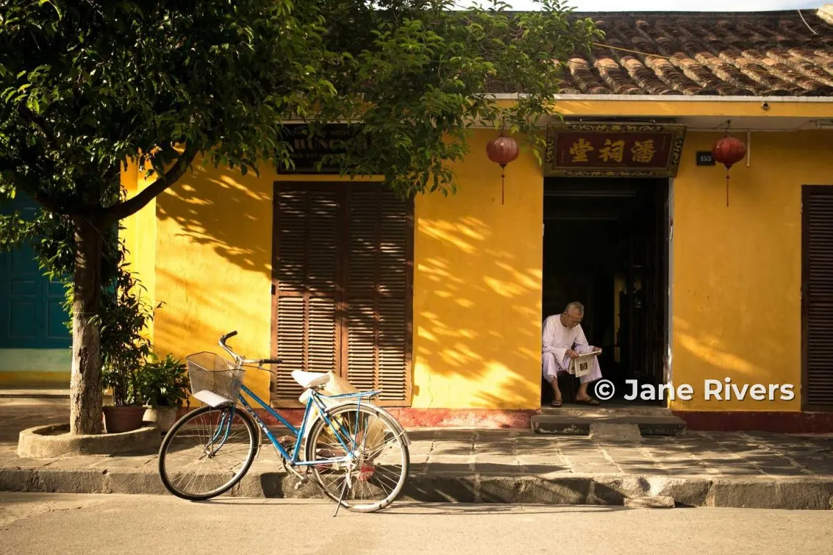 A yellow shopfront photo where the watermark covers a man sitting in the doorway