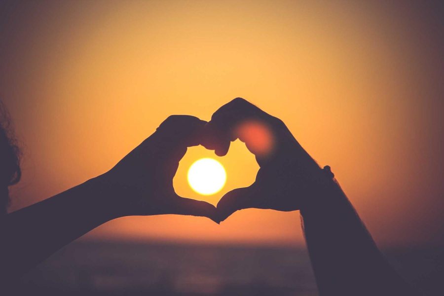 Two hands making a heart shape around the setting sun, with no watermark