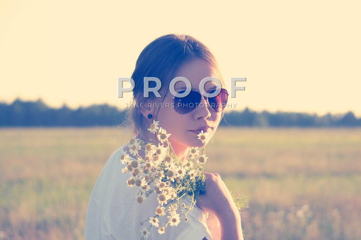 A woman in sunglasses holding flowers with the PROOF mark across her face