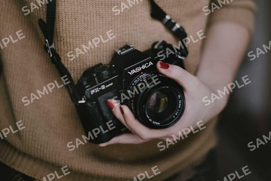 A photo of a person holding a film camera with SAMPLE repeated across it in white