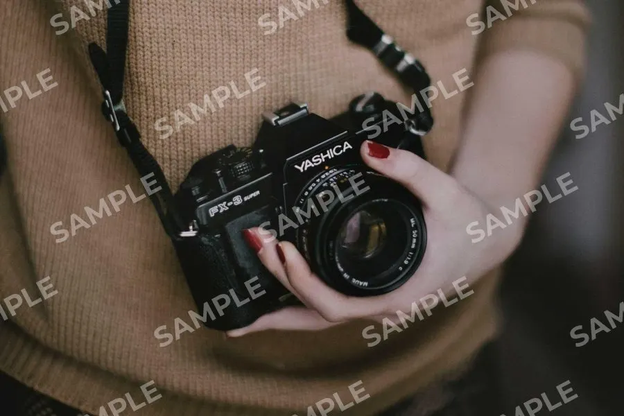 A photo of a person holding a film camera with SAMPLE repeated across it in white