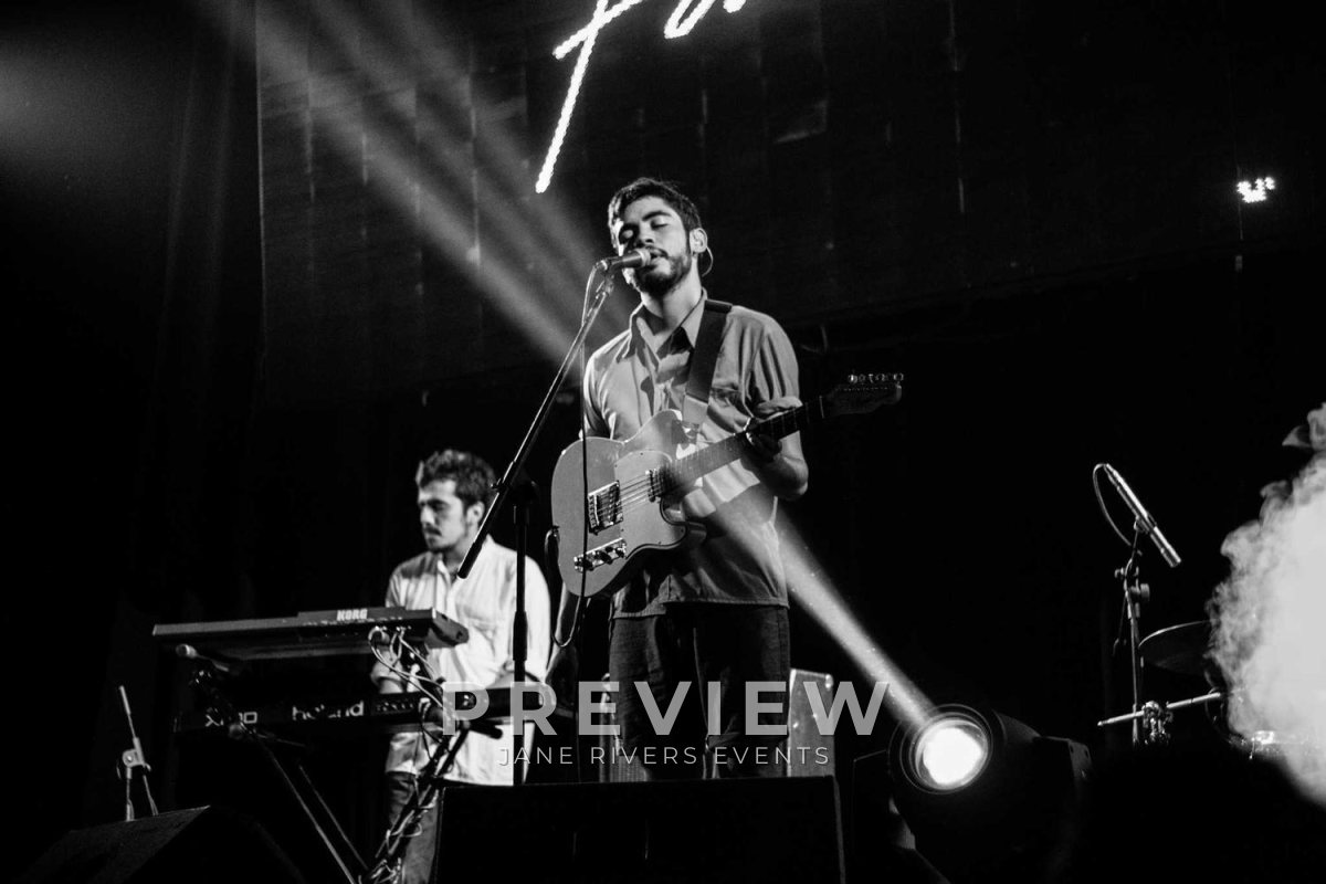 A black and white photo of a band on stage with a PREVIEW watermark below the musicians