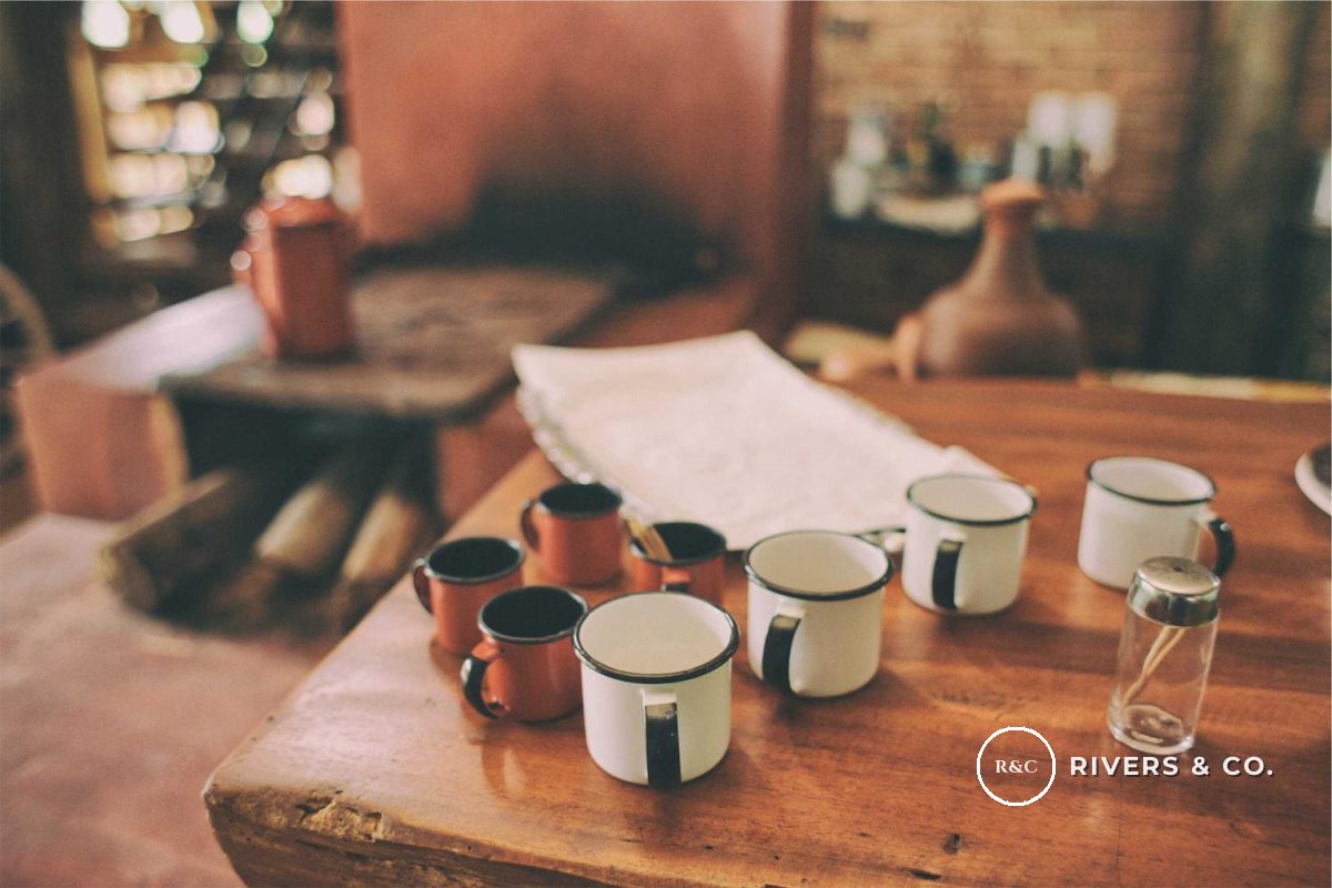 Enamel mugs on a café table with a small R&C monogram and RIVERS & CO. mark in the lower right
