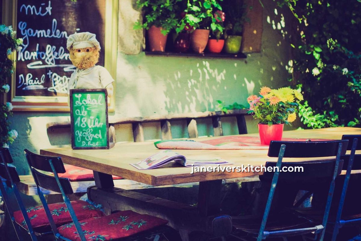 A café table with flowers and a chalkboard menu, with a small website watermark on the calm area beside the table