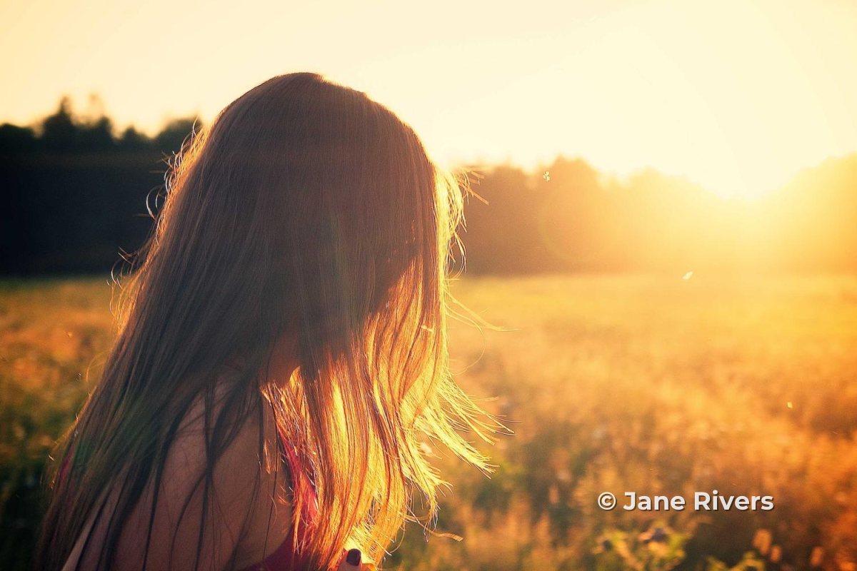 A girl in a golden field at sunset with a small © Jane Rivers credit in the lower right of the frame