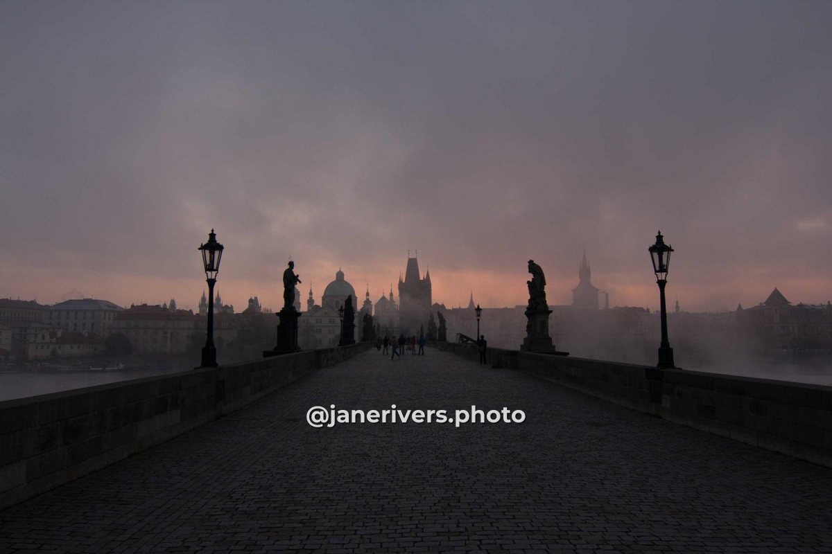 A misty bridge at dawn with @janerivers.photo written small in the lower third