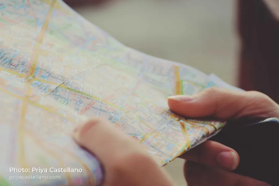 Hands holding a folded city map, with Photo: Priya Castellano and priyacastellano.com in small white text with a soft shadow in the lower left corner
