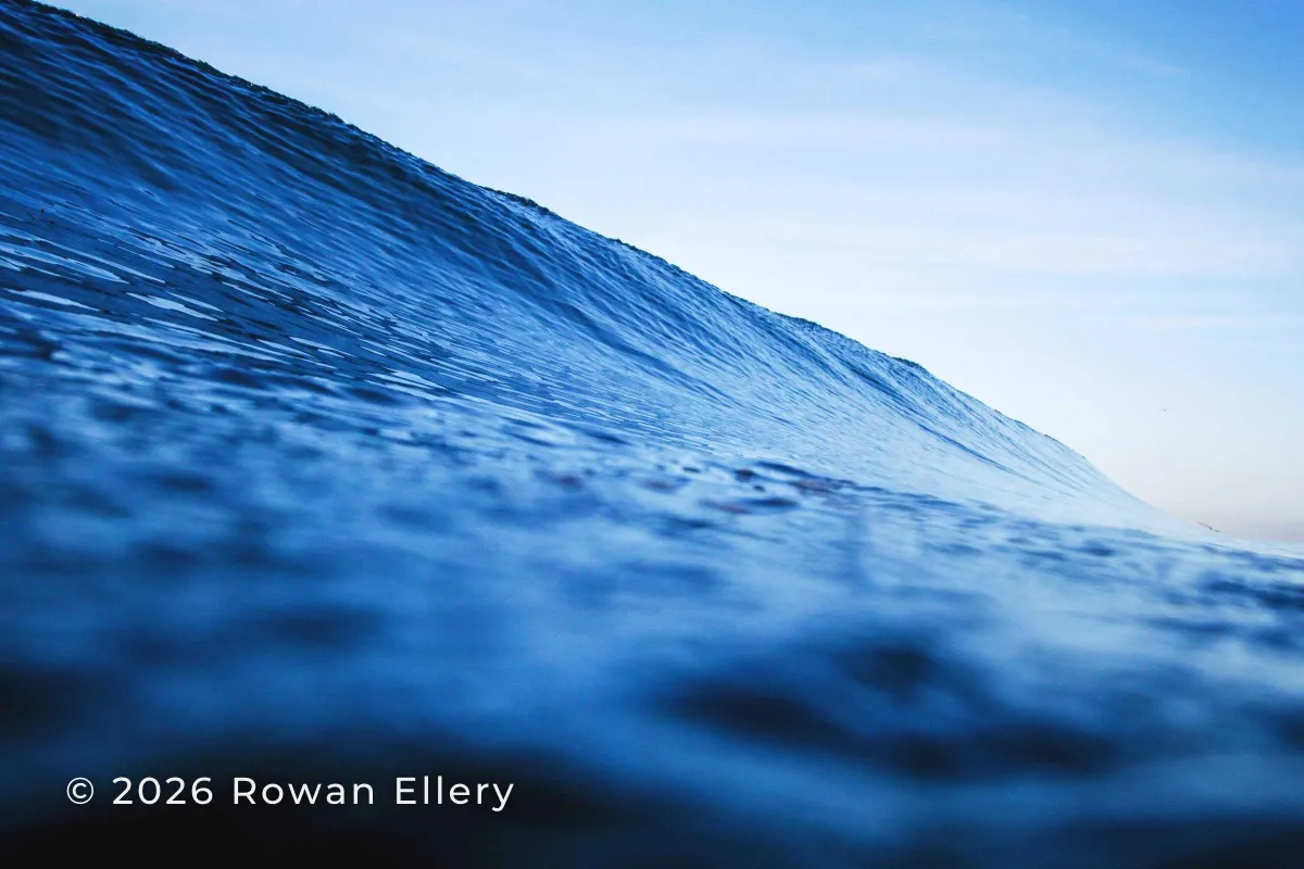 A close-up of a blue ocean wave with © 2026 Rowan Ellery in white in the lower left