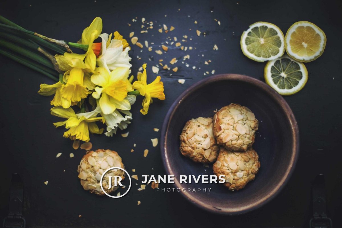 A flat lay of daffodils, lemon slices and cookies with a white JR monogram and the name Jane Rivers Photography in the lower left