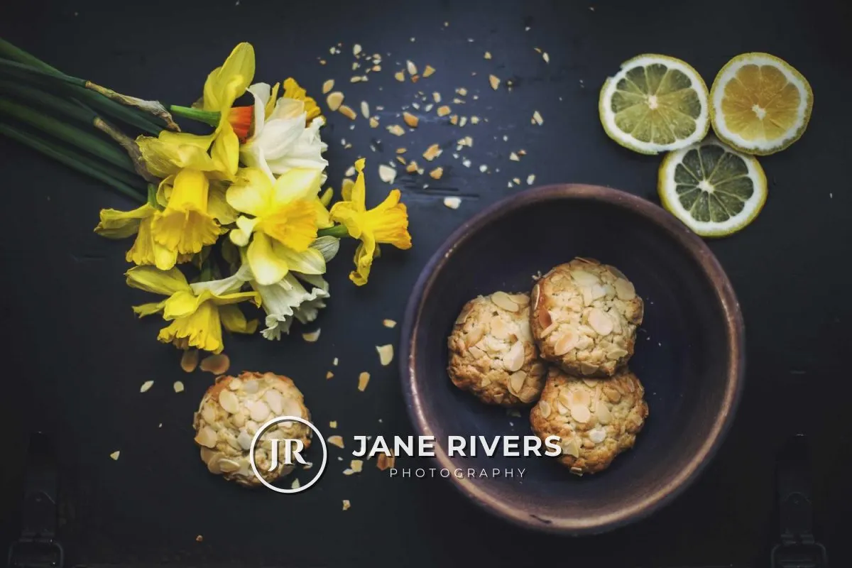 A flat lay of daffodils, lemon slices and cookies with a white JR monogram and the name Jane Rivers Photography in the lower left