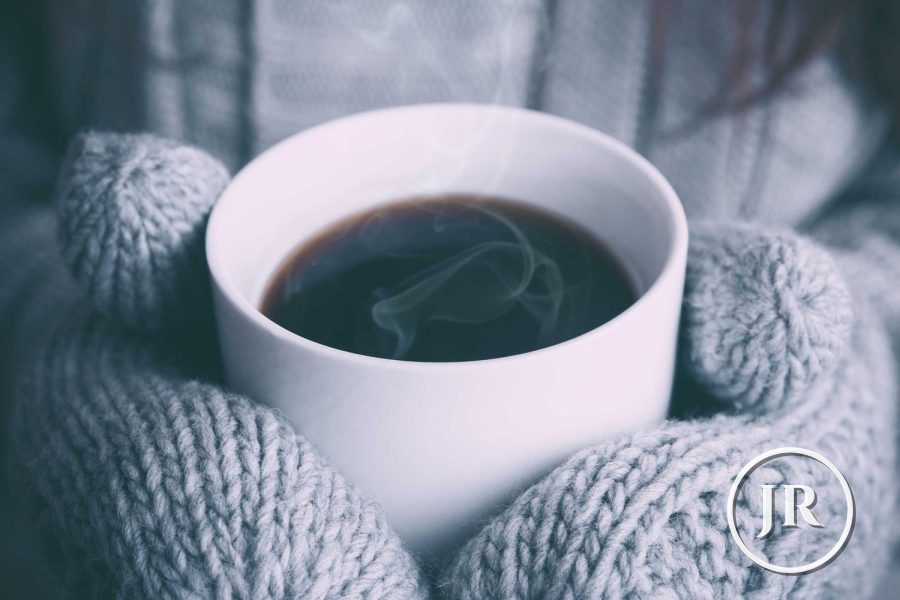 A coffee cup in knitted mittens with a small white JR logo in the corner