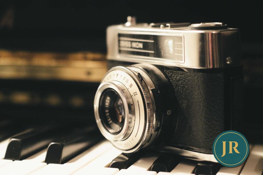 A vintage camera on piano keys with a small teal and gold JR logo in the corner