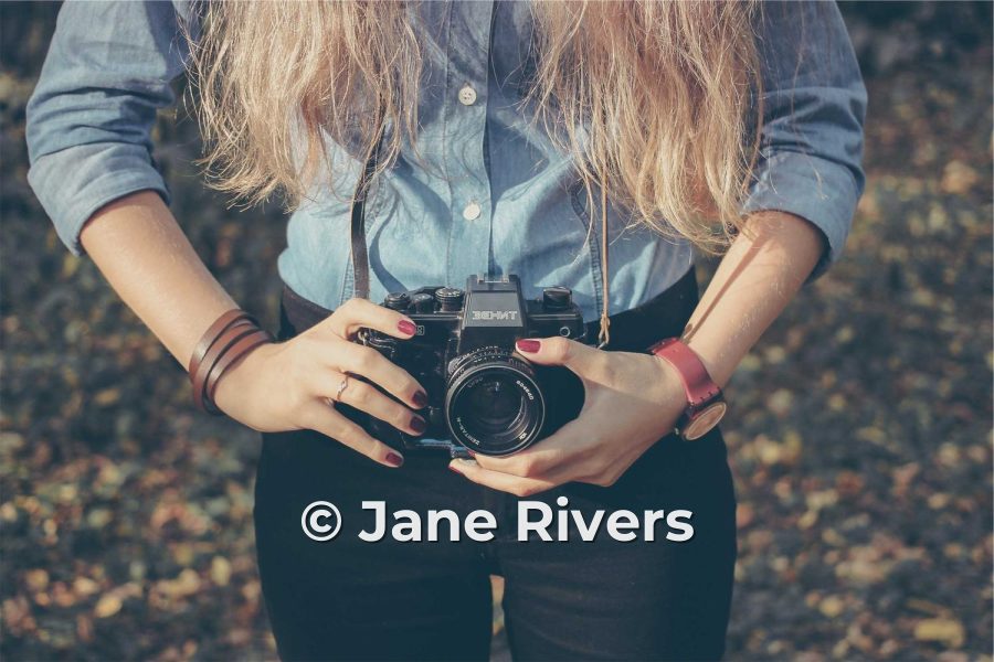 A woman holding a film camera with the watermark © Jane Rivers across her jeans