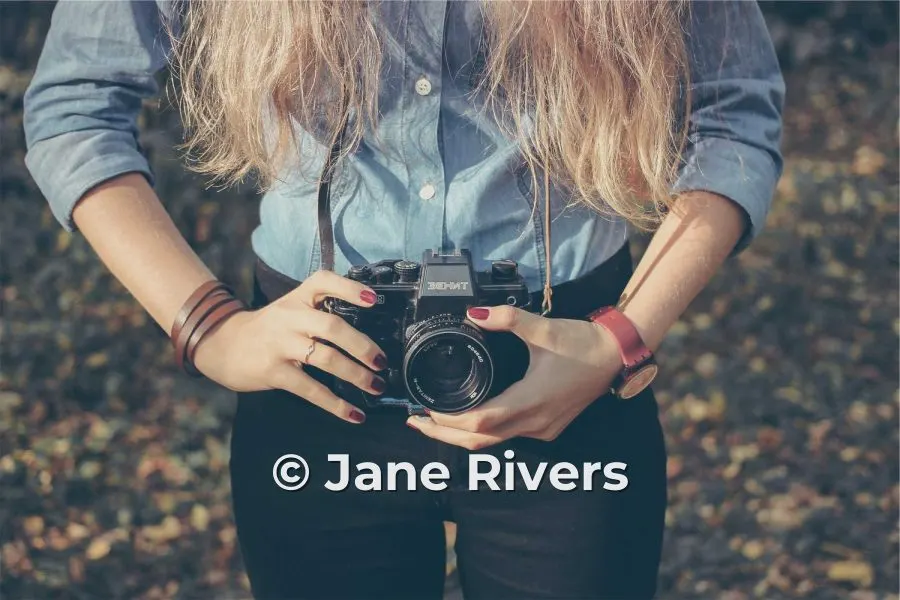 A woman holding a film camera with the watermark © Jane Rivers across her jeans