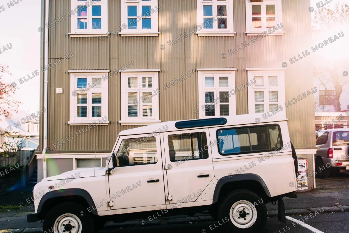 A white off-road vehicle parked in front of a corrugated metal house, covered by a faint tiled pattern of © ELLIS MOREAU in white letters with a thin dark outline
