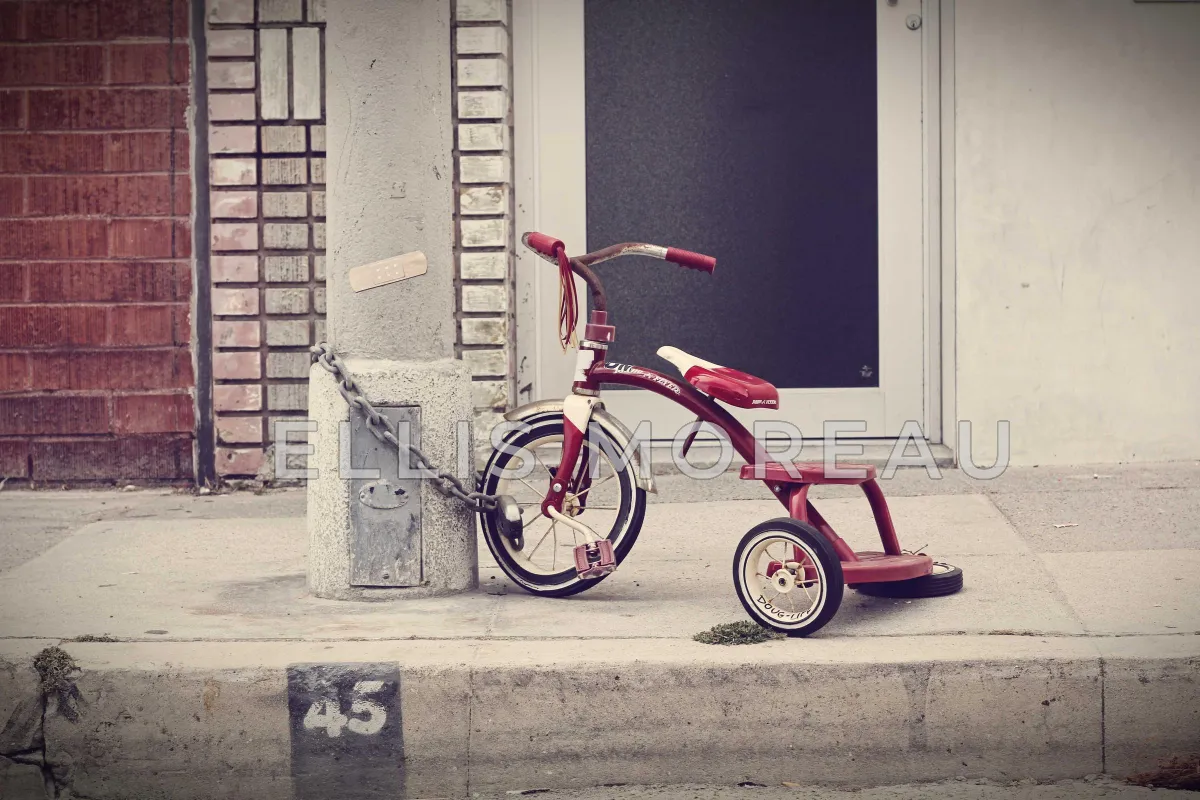 The same tricycle photo with ELLIS MOREAU in large, semi-transparent white letters running across the tricycle, its wheels and the pole