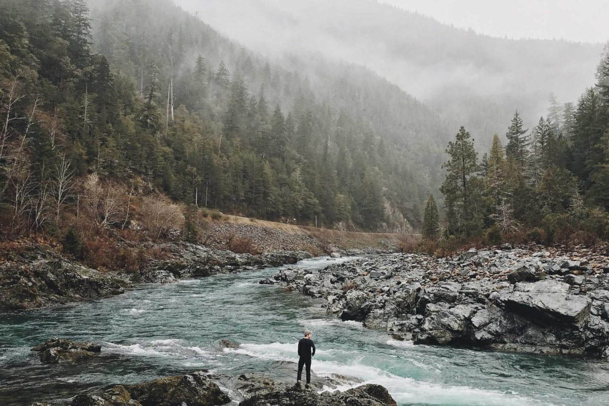 A misty river valley with a hiker standing on the rocks, with no watermark