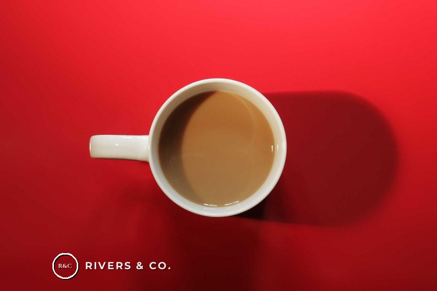 A cup of coffee on a red background with a small logo in the lower left