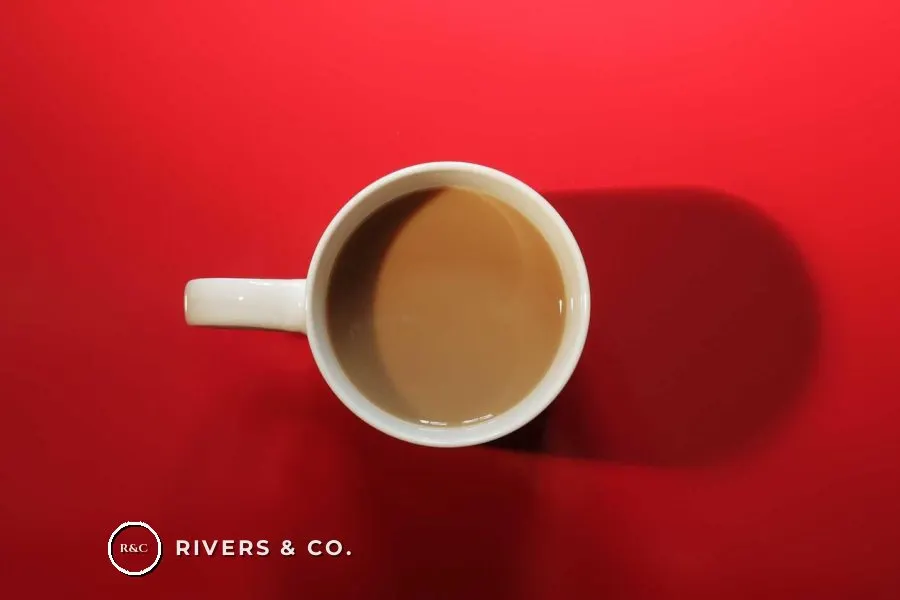 A cup of coffee on a red background with a small logo in the lower left