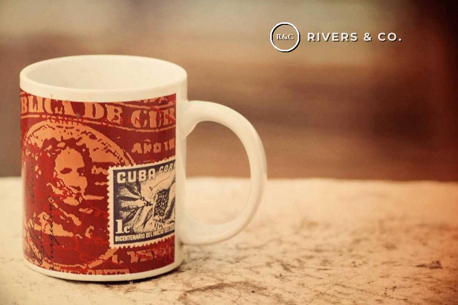 A patterned mug on a table with a small logo in the soft background at the top right