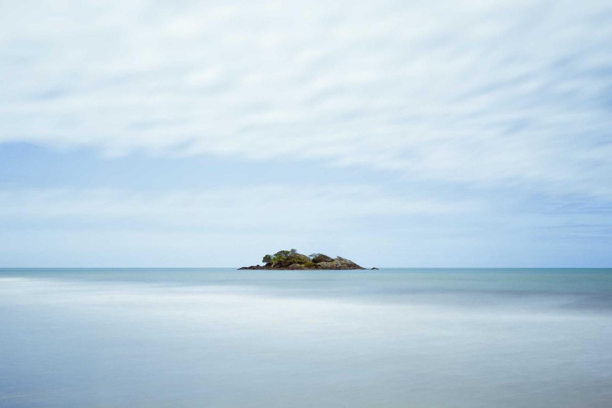 A calm seascape with a small island in the middle of a large area of sky and water