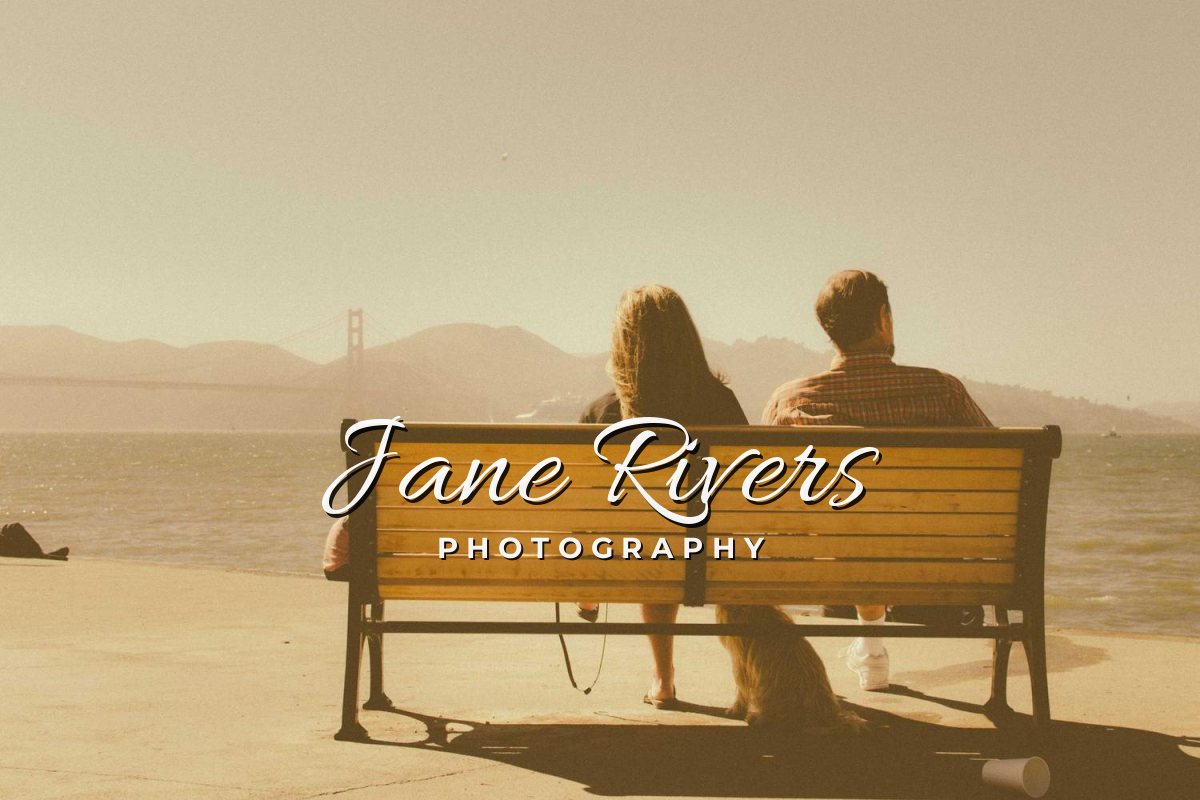 A couple on a bench by the sea with a handwritten Jane Rivers signature and the word Photography below it