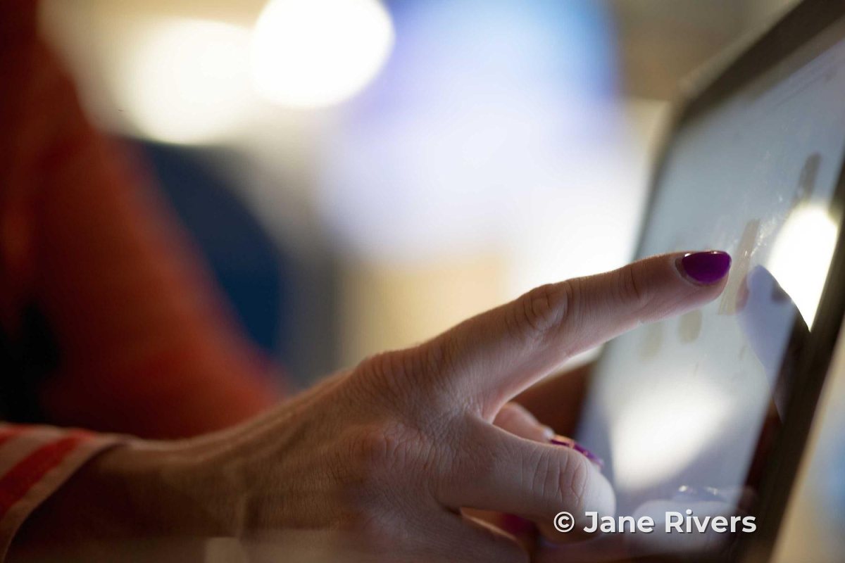 A finger scrolling through photos on a tablet screen, with a small copyright watermark in the corner