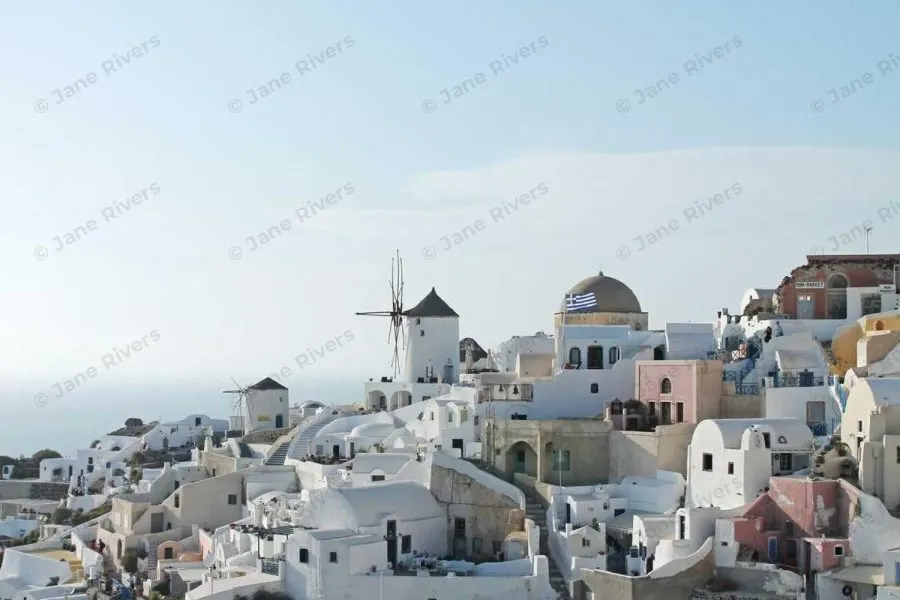 A white Greek village under a pale sky with a barely visible tiled watermark at 10% opacity