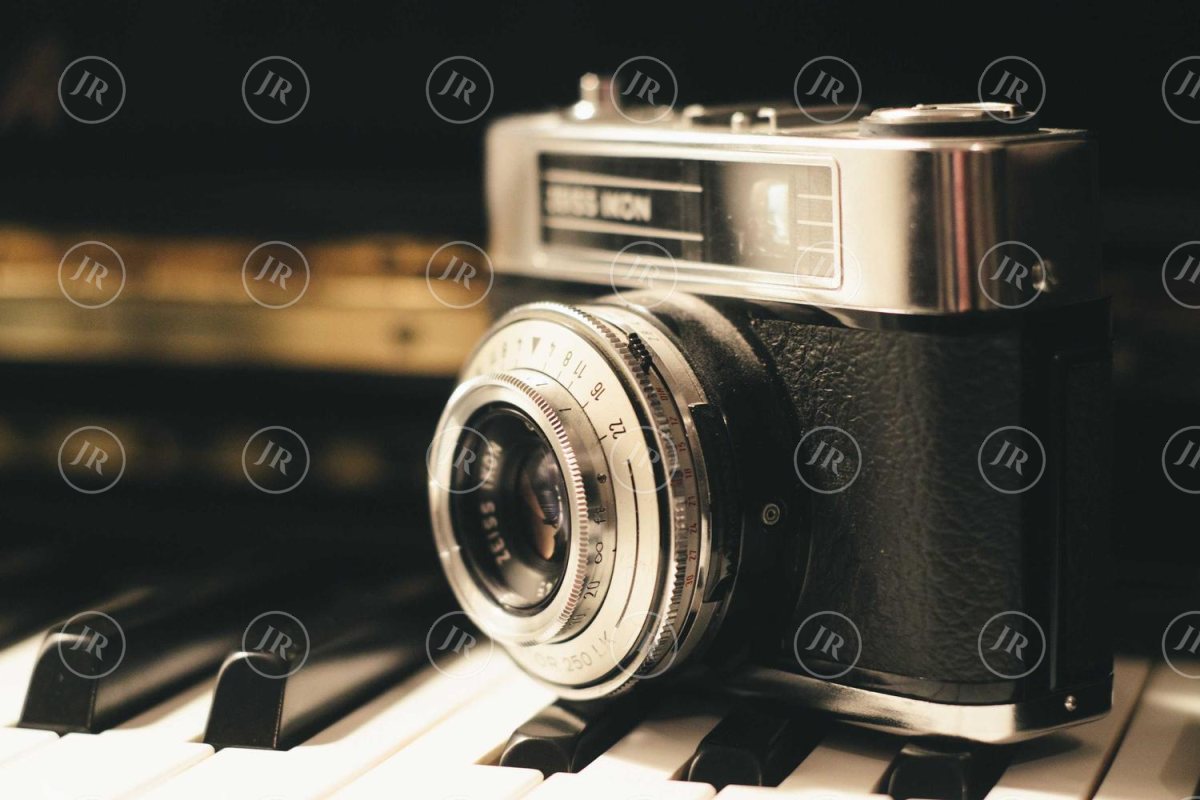 A vintage camera on piano keys with a faint pattern of small white circular JR logos