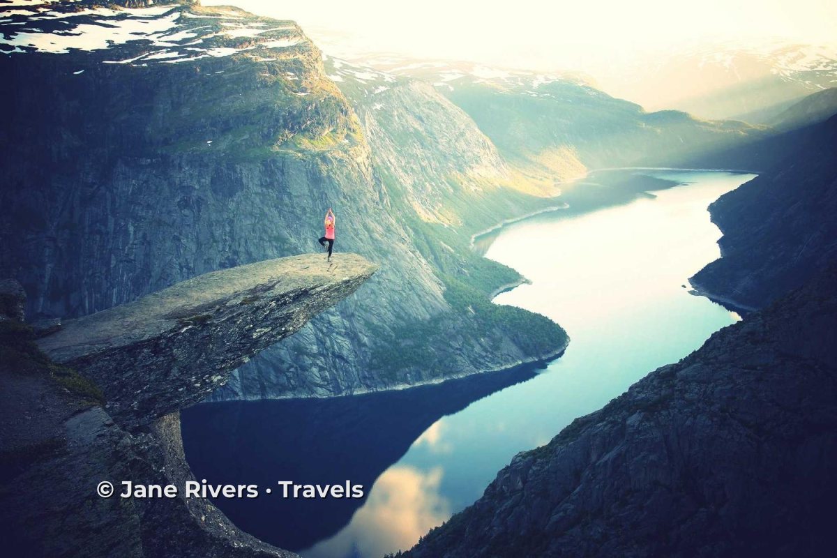 A hiker on a rock ledge above a fjord with a travel blog watermark on the cliff below