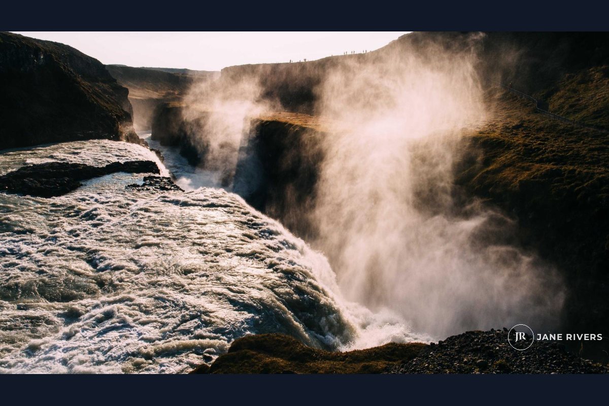A video frame of a waterfall in mist with a small monogram and name in the bottom-right corner