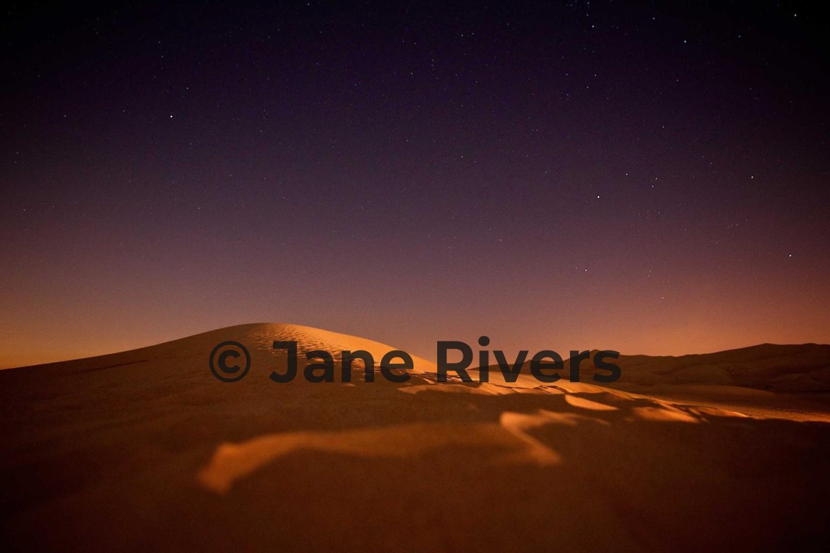 A desert dune at night with a black watermark that is hard to see