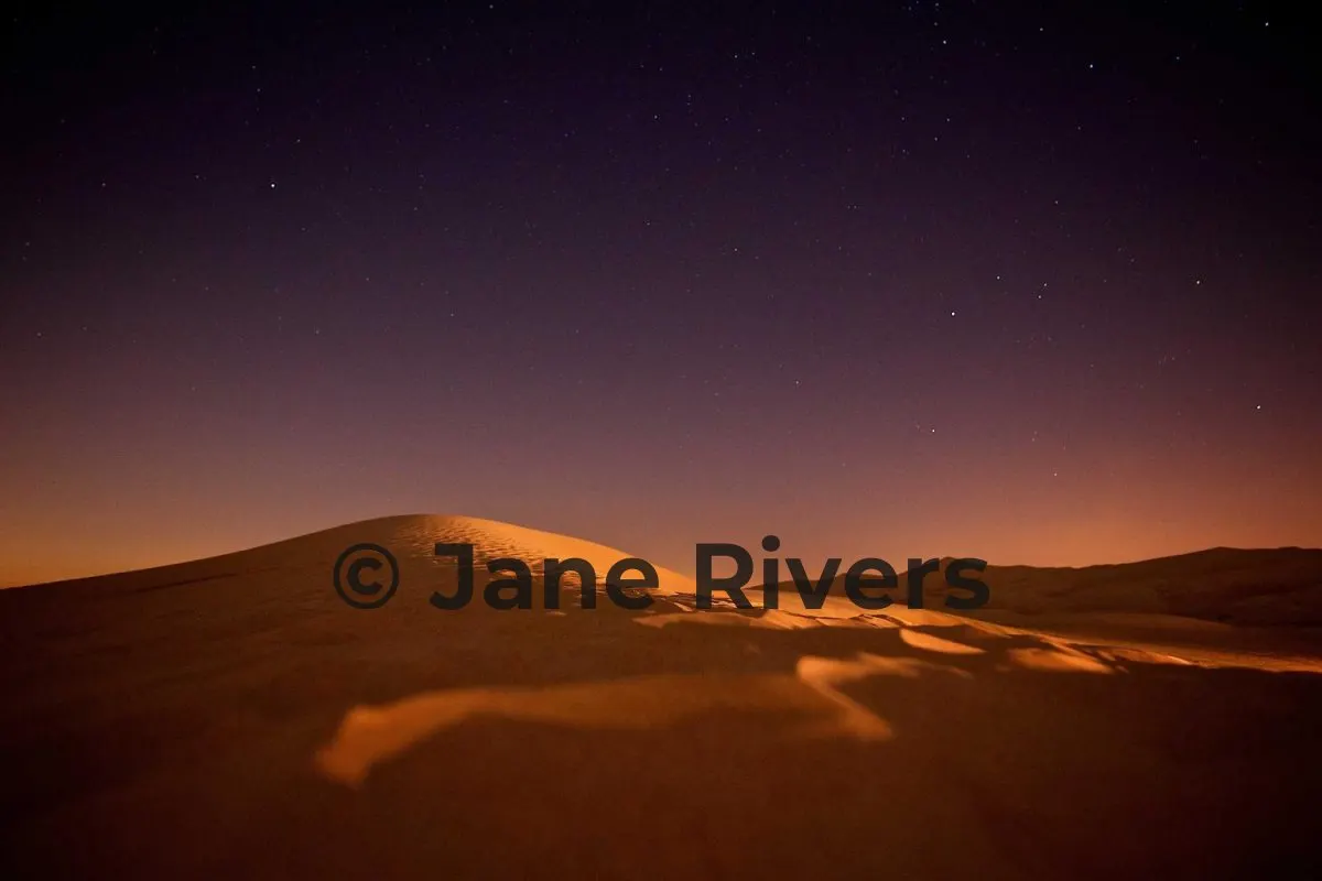 A desert dune at night with a black watermark that is hard to see