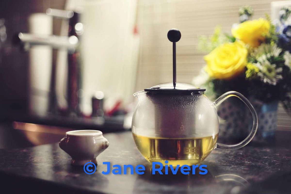 A warm photo of a glass teapot and yellow flowers with a bright blue watermark that clashes