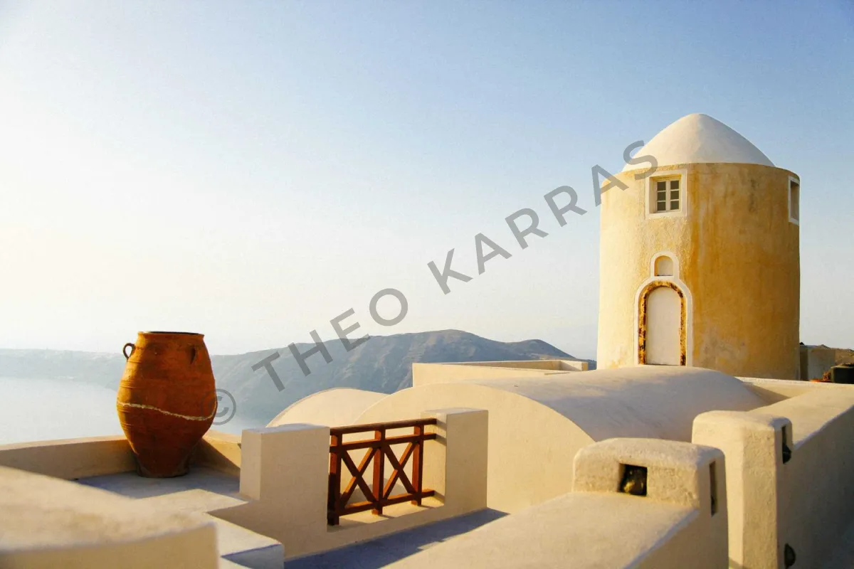 A whitewashed rooftop terrace on a Greek island with a clay urn and a round tower, crossed by © THEO KARRAS in large, faint dark letters running diagonally upward