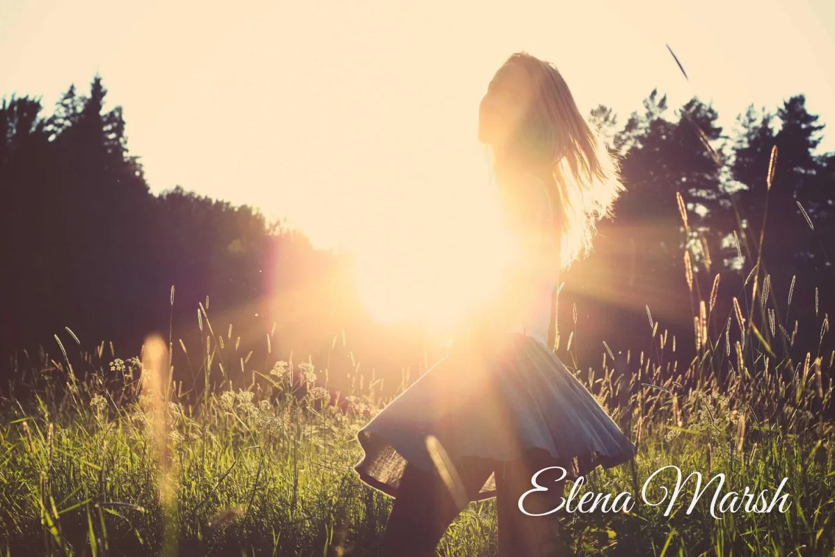 A woman twirling in a sunlit meadow at golden hour with Elena Marsh in a flowing white script signature in the lower right