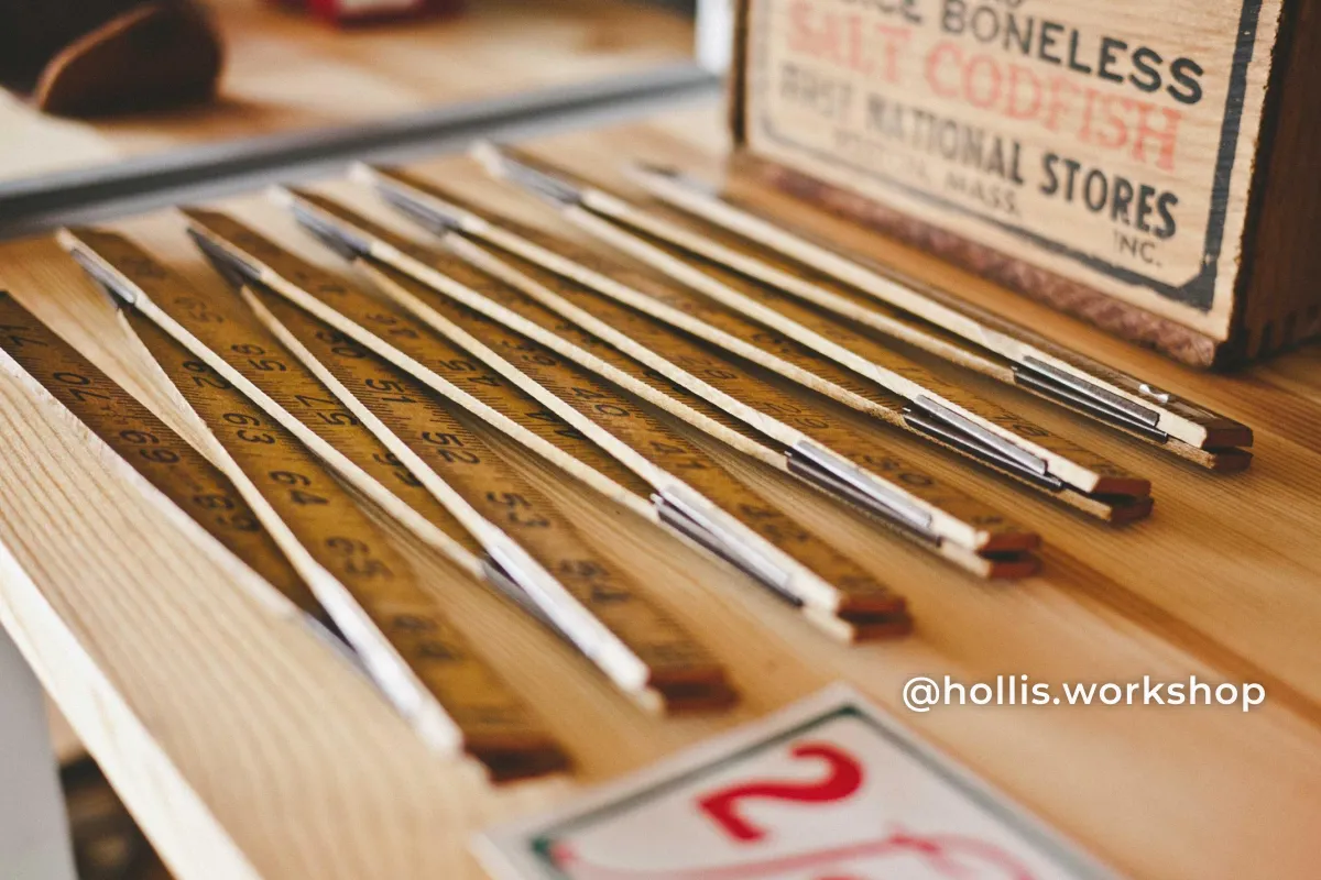 Vintage wooden folding rulers on a workbench, with @hollis.workshop in white in the lower right