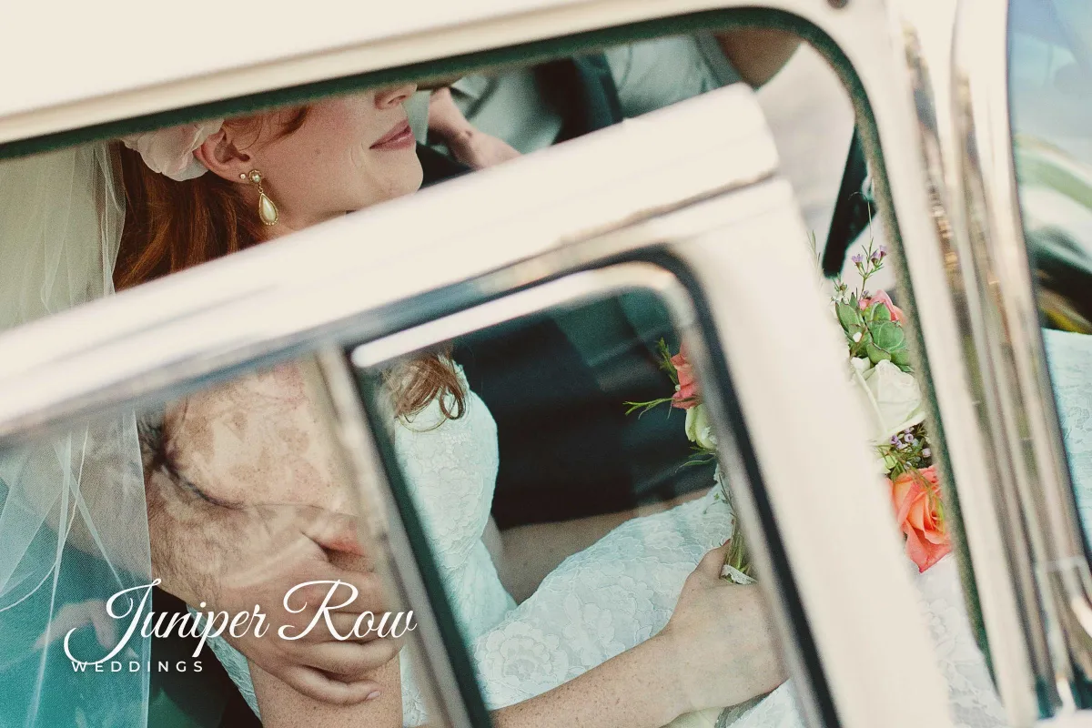A bride seen through the window of a vintage car, with Juniper Row in white script and WEDDINGS in small spaced capitals in the lower left