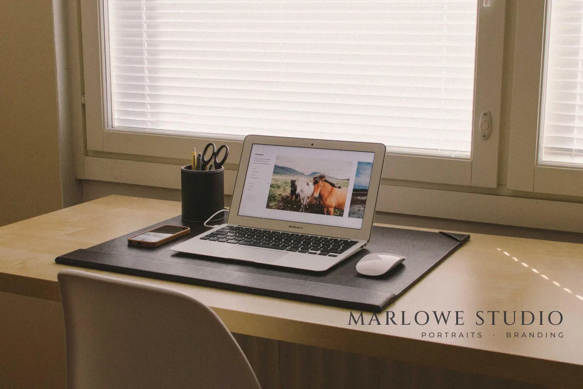 A desk by a window with a laptop, with MARLOWE STUDIO in dark serif capitals and PORTRAITS · BRANDING underneath on the desk in the lower right