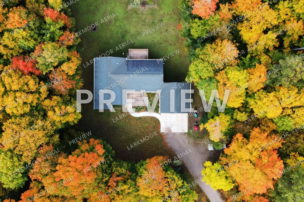 A top-down drone photo of a house with a blue roof surrounded by autumn trees, covered with a faint tiled LARKMOOR AERIAL PREVIEW pattern and a large PREVIEW across the middle