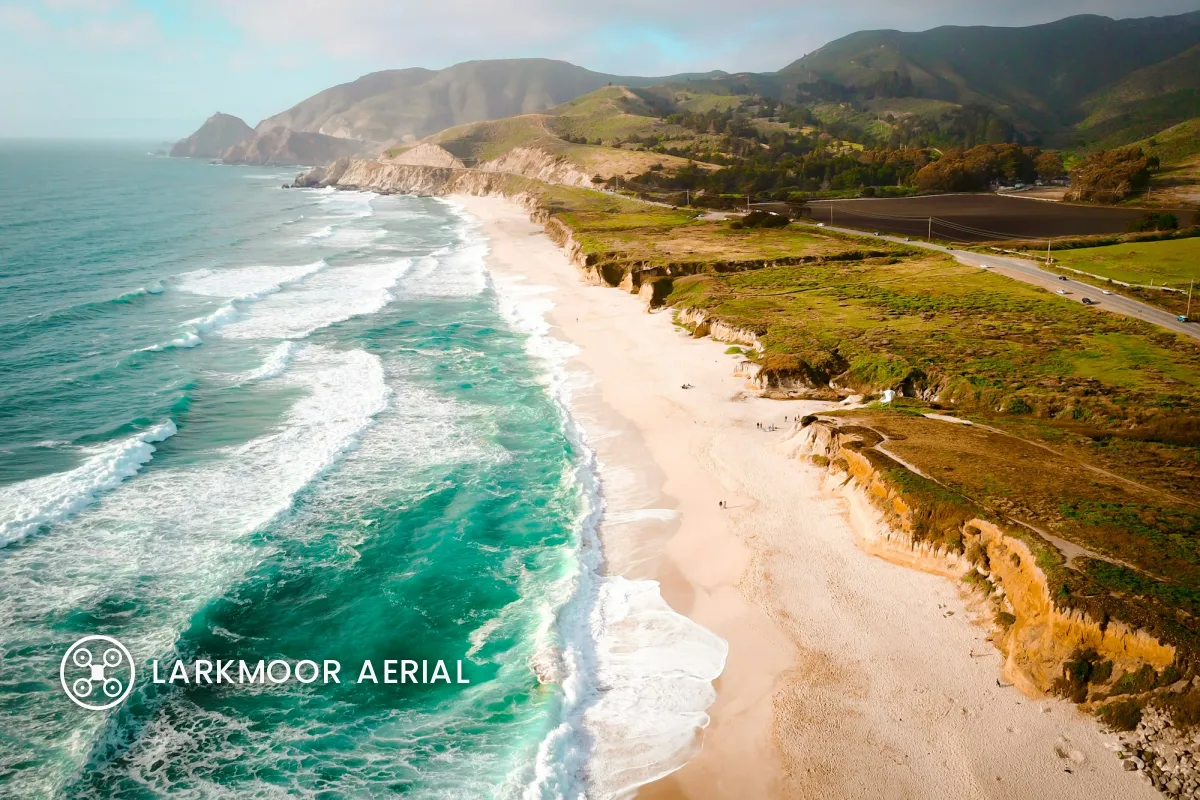 The same beach photo with the drone logo and LARKMOOR AERIAL set larger over the dark turquoise water on the left, with a soft shadow