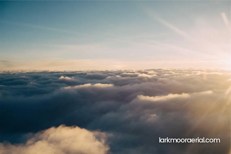 A view above a sea of clouds at sunrise with larkmooraerial.com in white in the lower right