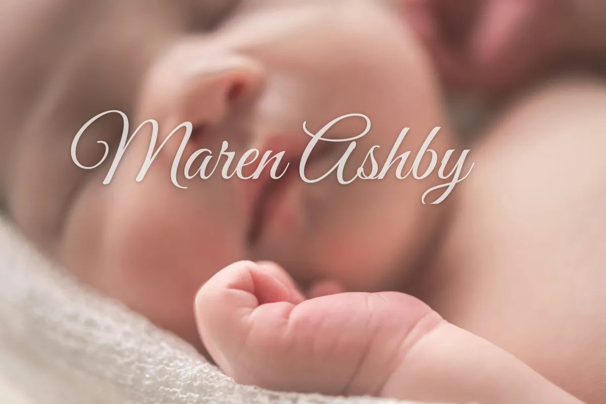 A close-up of a sleeping newborn with a large white script signature reading Maren Ashby across the baby's face