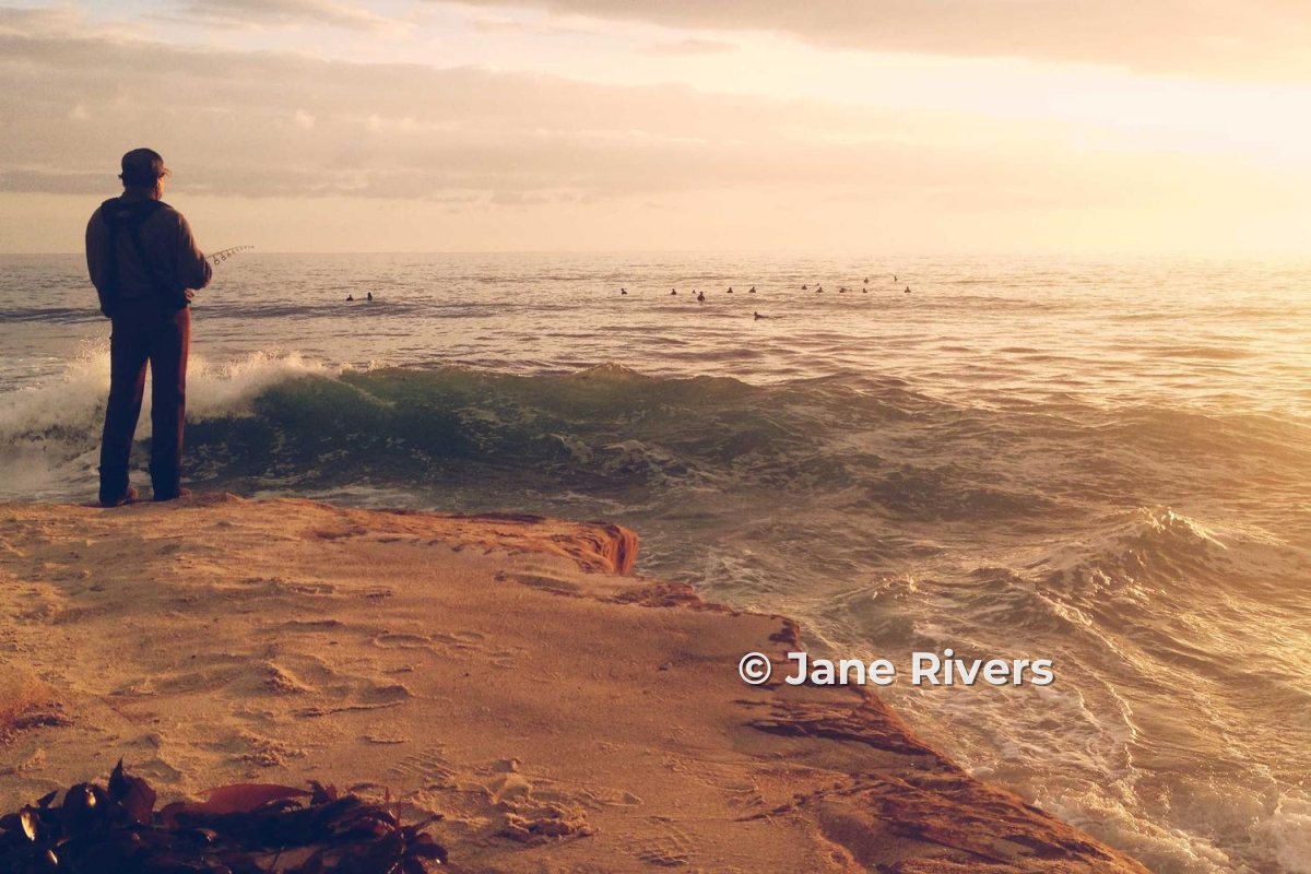 A person standing on a rocky coast at sunset, with a small copyright watermark in the lower right
