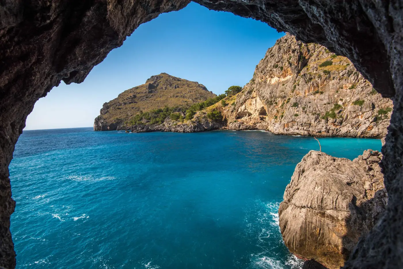 A sea arch over turquoise water with a handwritten signature watermark in the corner